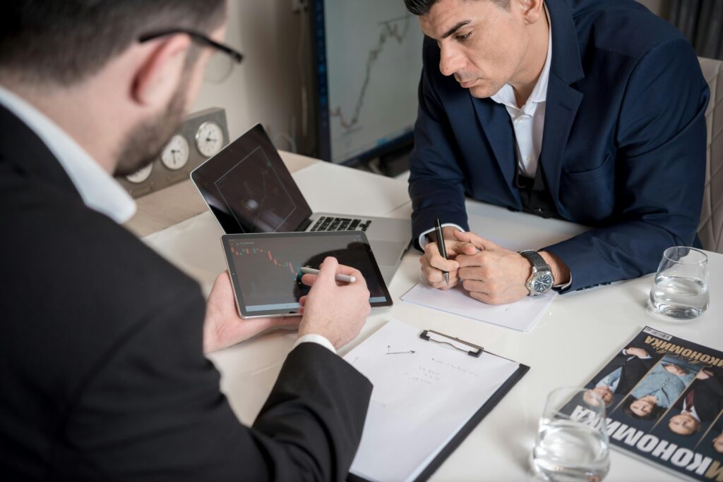 Two businessmen analyzing financial charts on digital devices in an office setting.
